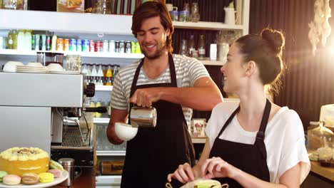 Camarera-Envolviendo-Sándwich-Mientras-El-Camarero-Vierte-Leche-En-Una-Taza