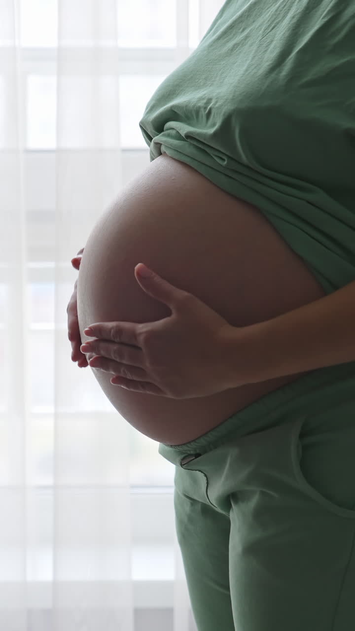 Pregnant woman standing near the window and relaxing at home. Maternity prenatal care and woman pregnancy concept Vertical video