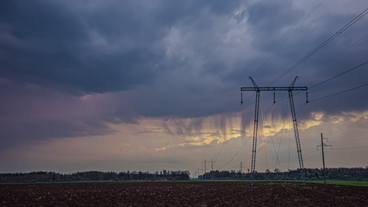 Timelapse shot of dark rain clouds passing by over freshly ploughed farmlands alongside electric lines during evening time