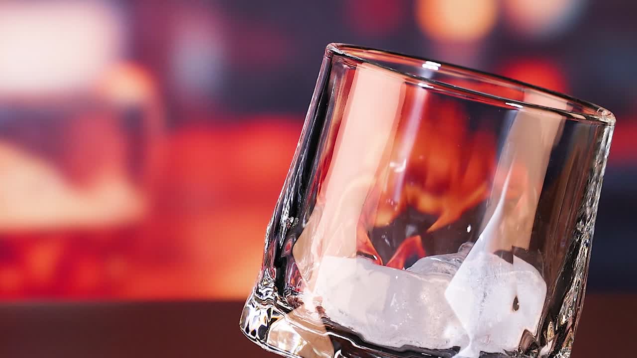 Close-up of ice cubes being dropped into a tilted empty glass against a blurred background.