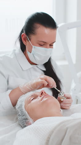 beautician applying moisturizing medical chemical peeling acid mask on young woman face and eyes