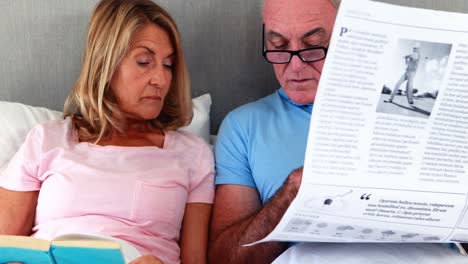 pareja de mayores en la cama leyendo periódicos y libros