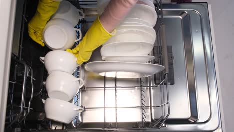 person in yellow gloves loading a dishwasher with white dishes
