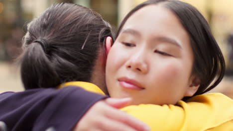 close up of two smiling young female friends meeting and hugging in urban setting together 2