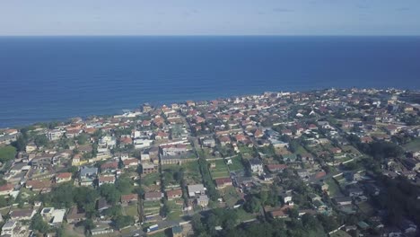 Drone-flying-over-residential-homes-moving-towards-the-ocean-on-a-clear-blue-day-with-good-visibility