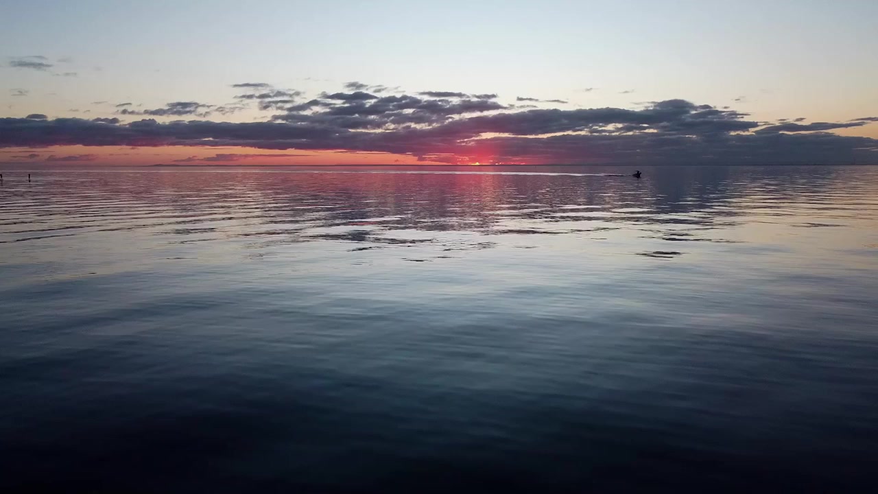 A smooth pan up to a boat at sunset, capturing the warm glow of the sky and the serene atmosphere of the water as the day ends.