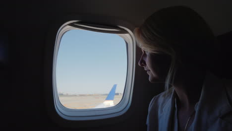 una mujer joven mira por la ventana del avión que comienza a acelerar a lo largo de la pista de inicio de