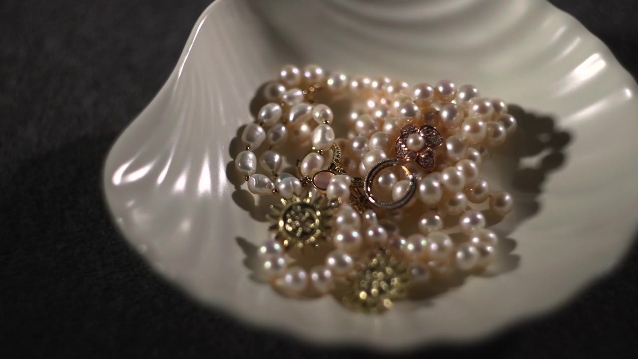 Ciondolo a raggiera su collana di perle in ciotola di conchiglia. Dettaglio focalizzato con anello e motivi floreali. Ombra da studio.
