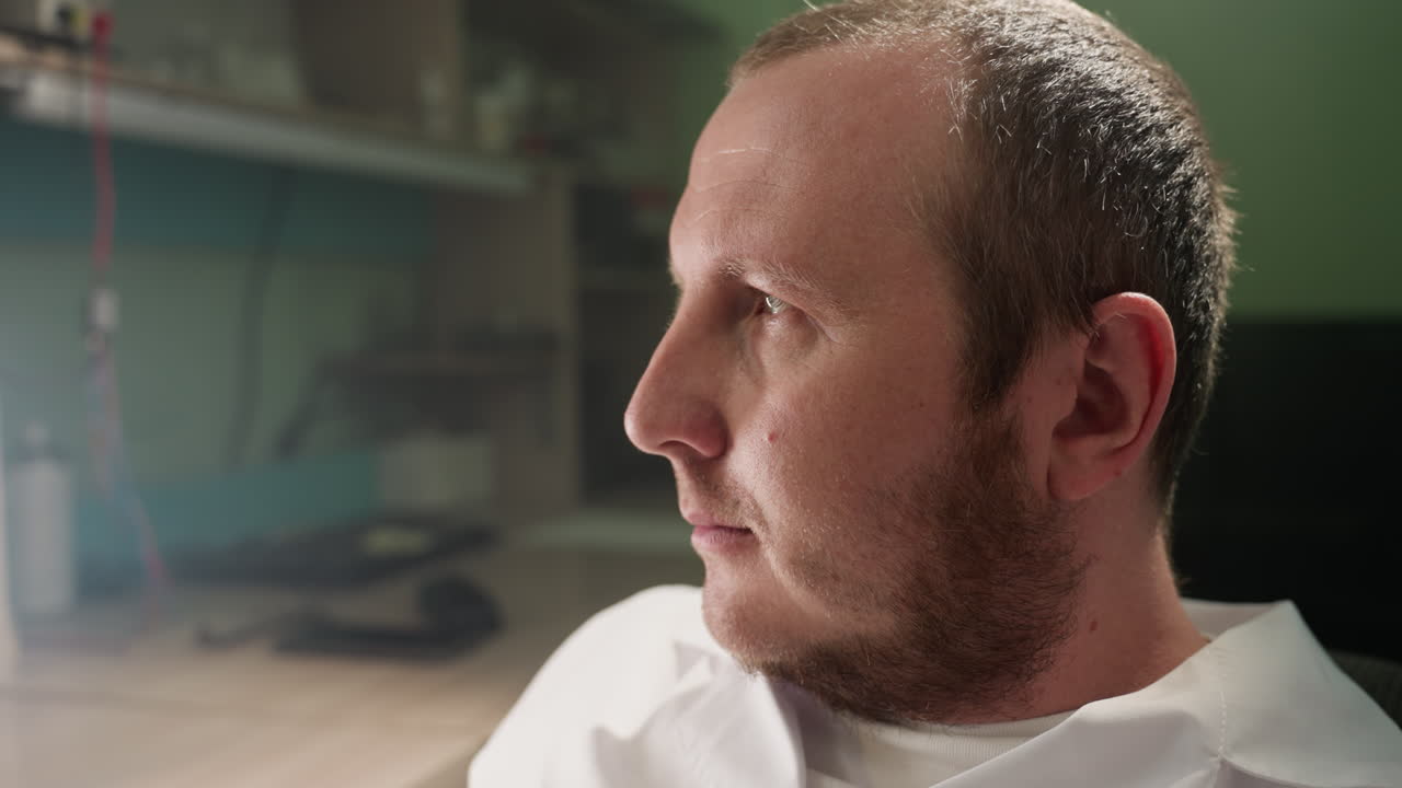 색 실험실 코트를 입은 기술자의 클로즈업 뷰, 그의 작업실에 깊이 집중, 기술자의 얼굴은 흐릿한 배경에 실험실 장비와 함께 집중을 반영합니다.