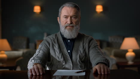 Portrait-of-senior-man-sitting-at-table-with-crossed-hands-in-vintage-cabinet.