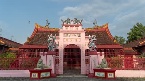 a vibrant pink and red traditional chinese temple with ornate statues and a grand entrance gate