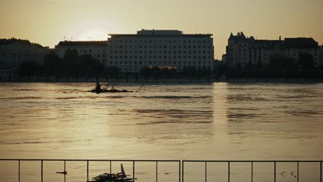 debris floating down the danube at sunset with buildings silhouetted in the background during budapest flood 2024