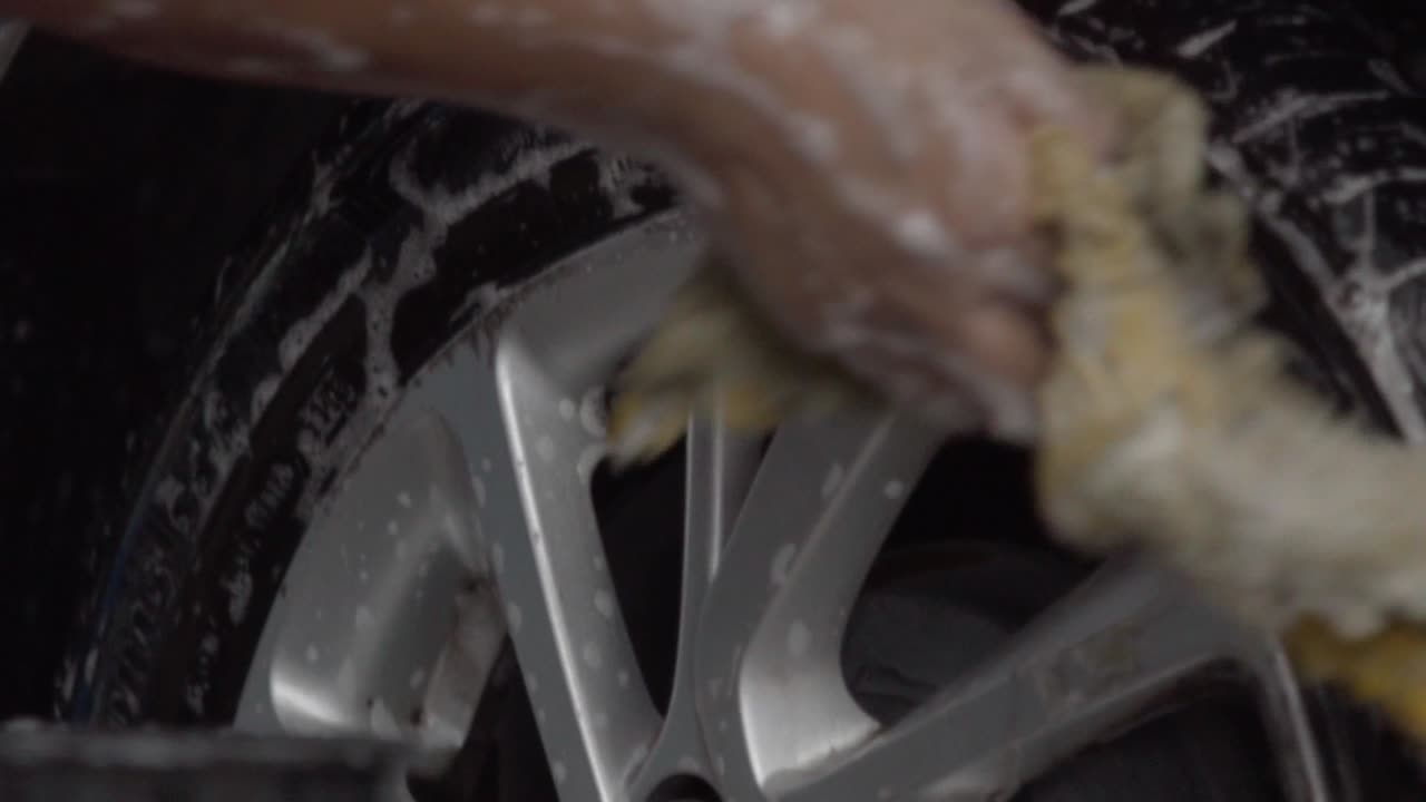 Close up of washing the front of a car tire with foam and pressurized water. Car wash.