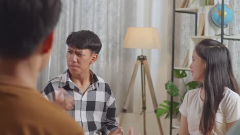 asian teen group sitting in chairs forming a circle in conflict trying to blame each other. close up of a boy in plaid shirt arguing with a girl