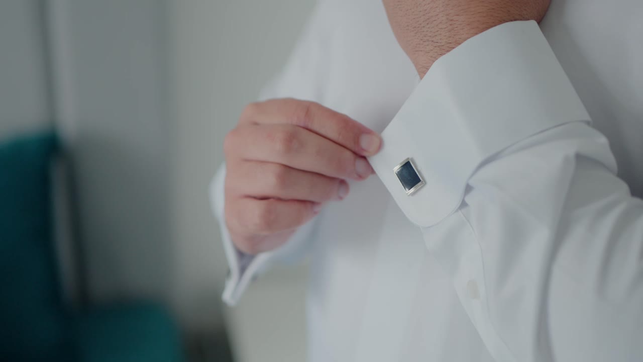 Close up of a man adjusting his cufflink on a crisp white dress shirt before an event
