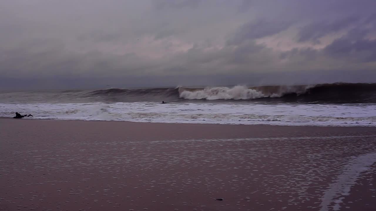 Ocean day time; Few men are swimming; Purple light fills air; grey and blue clouds in a sky are formed and feel stationary. It is a bright and partially sunny day. Cornwall, UK. Filmed in HD
