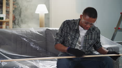 hombre afroamericano puliendo tabla de madera sentado en el sofá