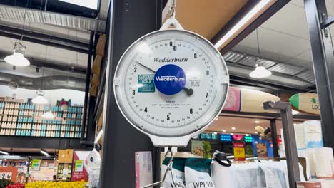 a person places cauliflower on a scale in a grocery store. bright lighting and organized shelves create a vibrant atmosphere