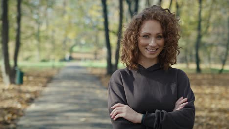 Portrait-of-smiling-ginger-woman-standing-and-looking-in-camera-side-in-park