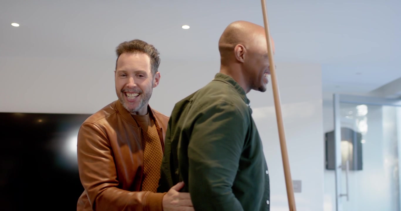Diverse mannen in een speelkamer die elkaar aanstoten, zich omdraaien naar de biljarttafel, een keu pakken om te spelen, met ruimte voor tekst.
