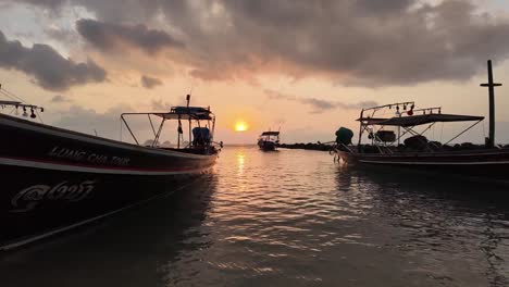 Two-Fishing-Boats-Rocking-in-Boat-Harbor-as-Waves-Ripple-to-Shore,-Beautiful-Sunset-in-Thailand