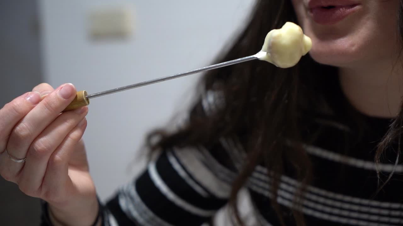 joven linda comiendo fondue, un plato de queso derretido suizo servido en una olla comunal sobre una estufa portátil calentada con una vela y comido sumergiendo pan en el queso usando tenedores largos
