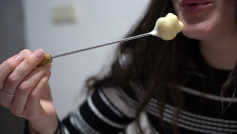 Young-cute-girl-eating-fondue,-a-Swiss-melted-cheese-dish-served-in-a-communal-pot-over-a-portable-stove-heated-with-a-candle-and-eaten-by-dipping-bread-into-the-cheese-using-long-forks