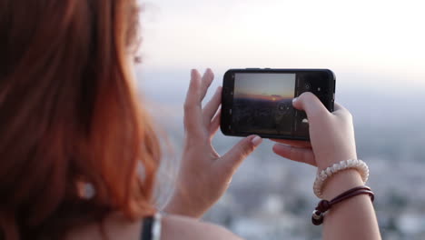 woman taking a picture of a sunset with her smartphone