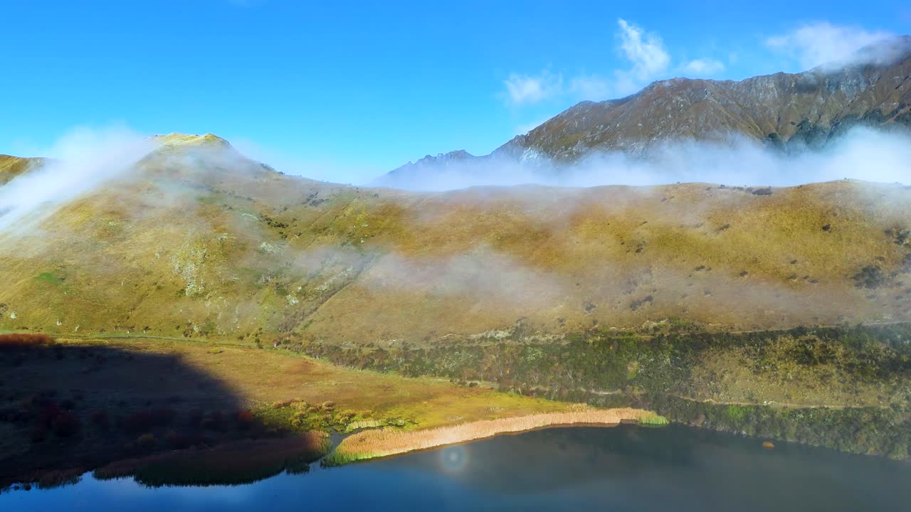 A serene landscape with a rainbow over Moke Lake, surrounded by mist and mountains under clear blue skies