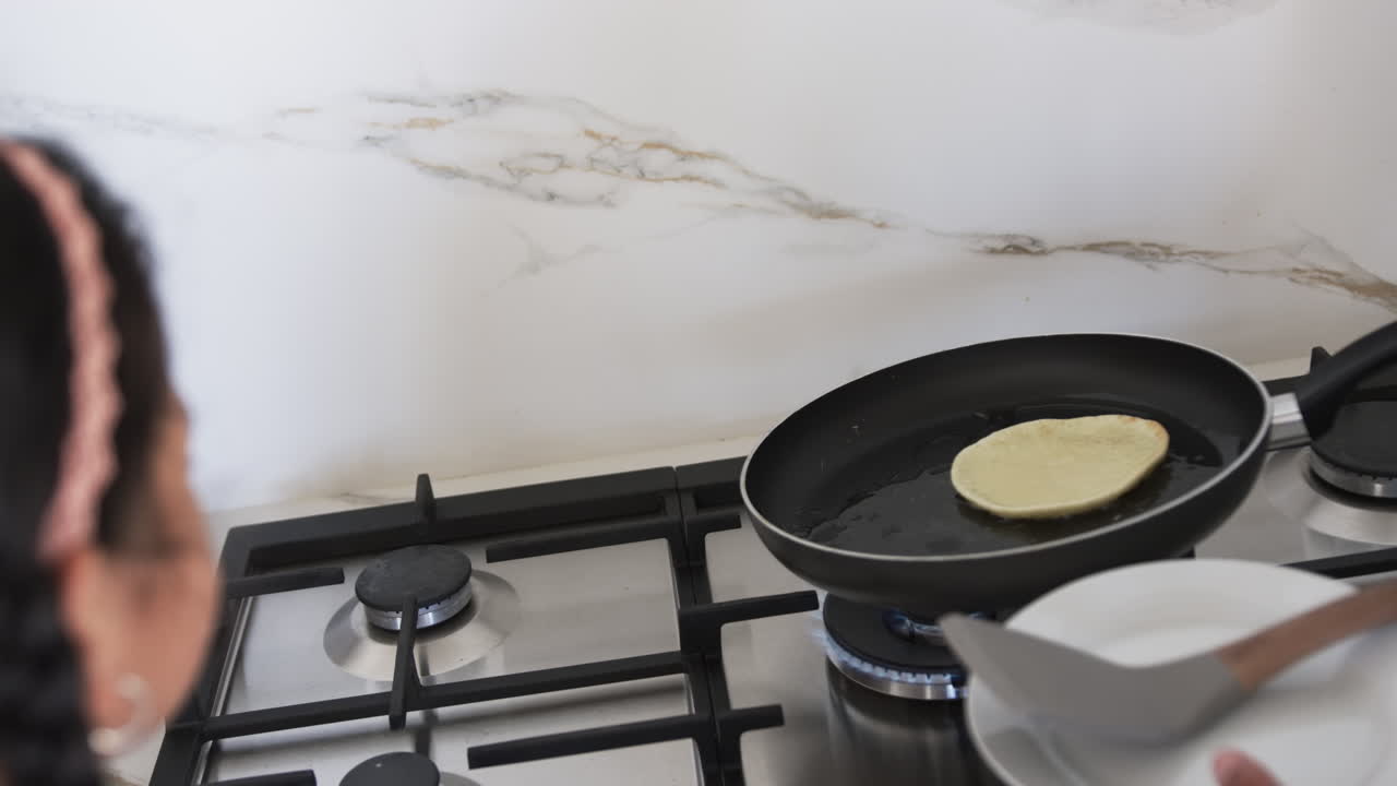 Una donna birazziale sta cucinando pancake su un fornello, con un focus sulla padella