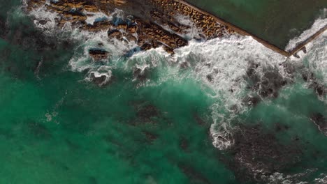 aerial drone view zooming out as waves rolling in crashing over rocks