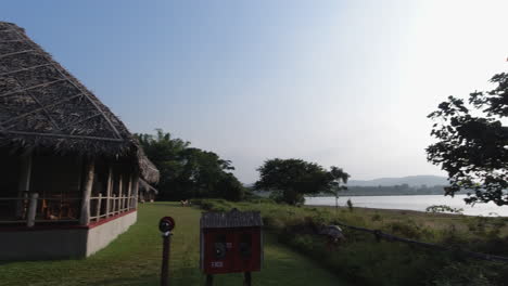 a peaceful riverside resort with a thatched hut, trees, and calm kabini river water in the distance