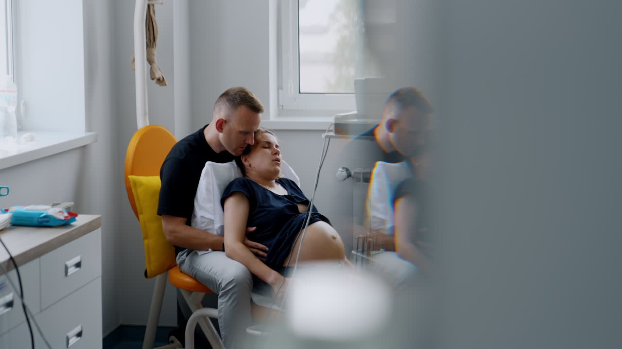 Caucasian man comforting his wife during childbirth. Tired woman lies in his arms breathing slowly.