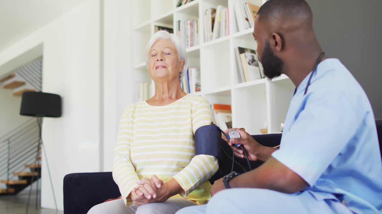 Video of happy african american male doctor checking pressure to caucasian senior woman