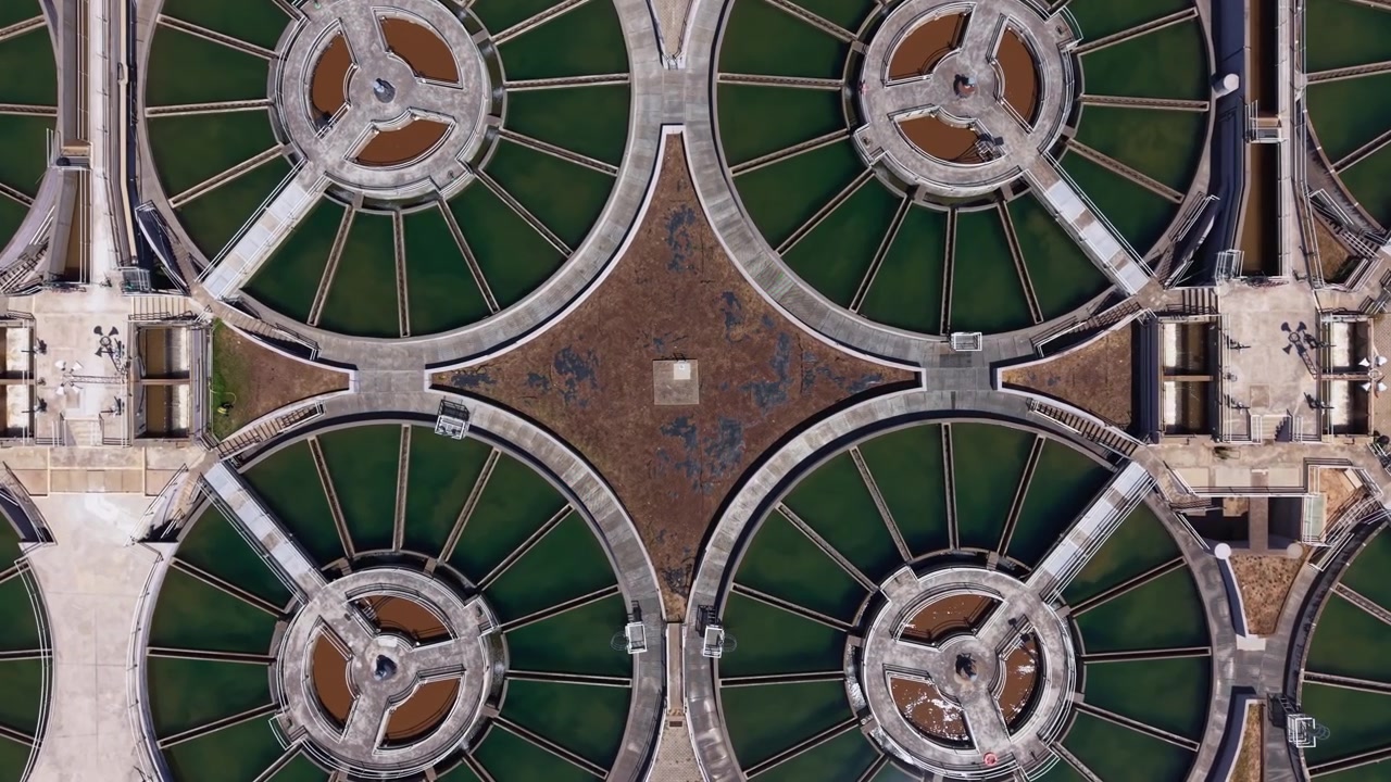 Vista aérea de clarificadores de floculación circulares conectados por pasarelas radiales en una planta de tratamiento de agua potable, formando patrones geométricos con agua verde.