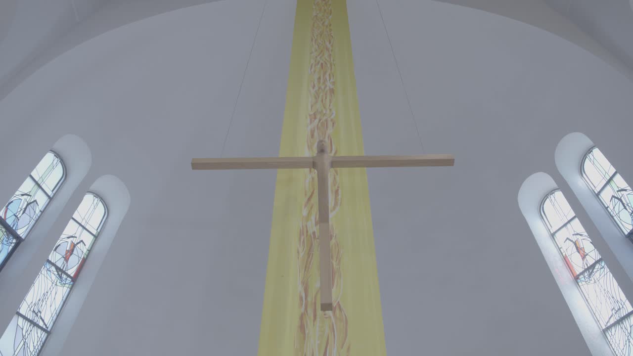 A wooden cross hangs in front of a yellow banner in a church, camera pan from top to bottom