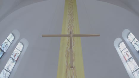 a wooden cross hangs in front of a yellow banner in a church, camera pan from top to bottom