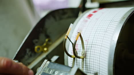 Male hand touching the seismological device where a needle drew a red line on graph measuring activity. Equipment used at gas or oil drilling process. Close up.