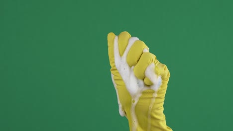 woman hand in yellow protective rubber glove squeezes blue cleaning sponge over green background. 4k video