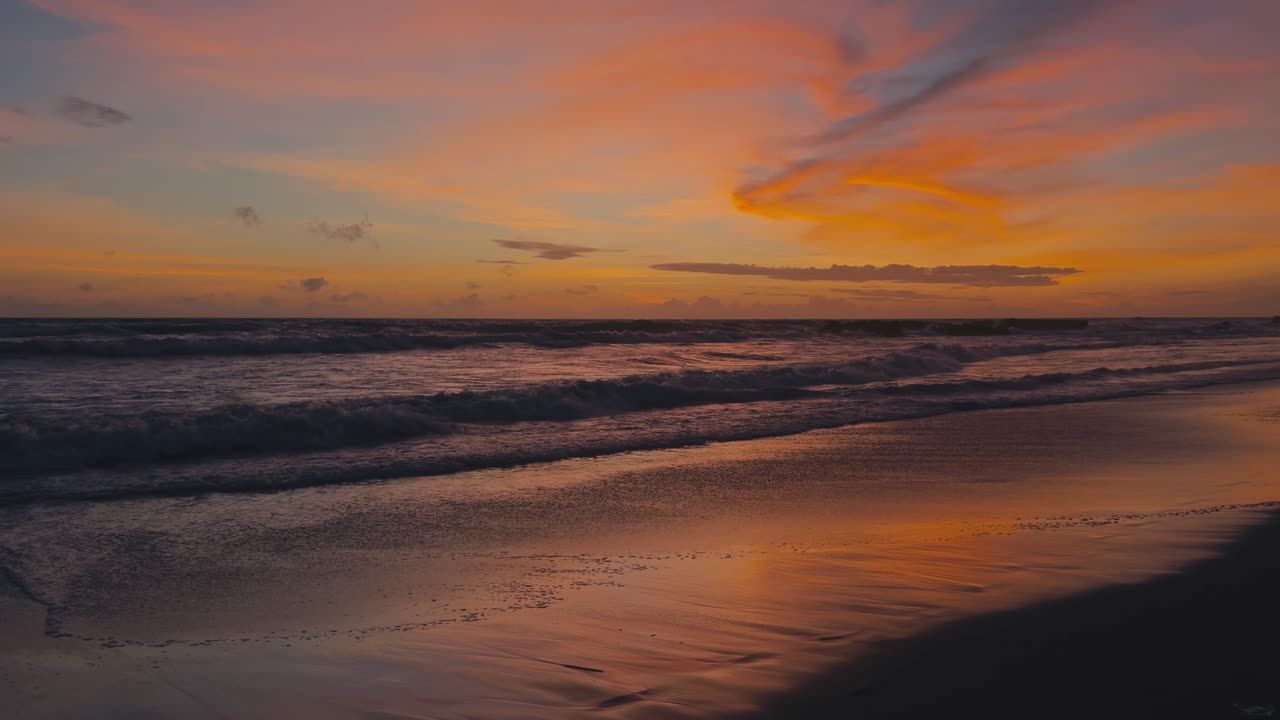 Stunning sunset with vivid orange and red tones reflecting on calm ocean water and wet sand. Peaceful coastal scene with warm light and serene evening atmosphere