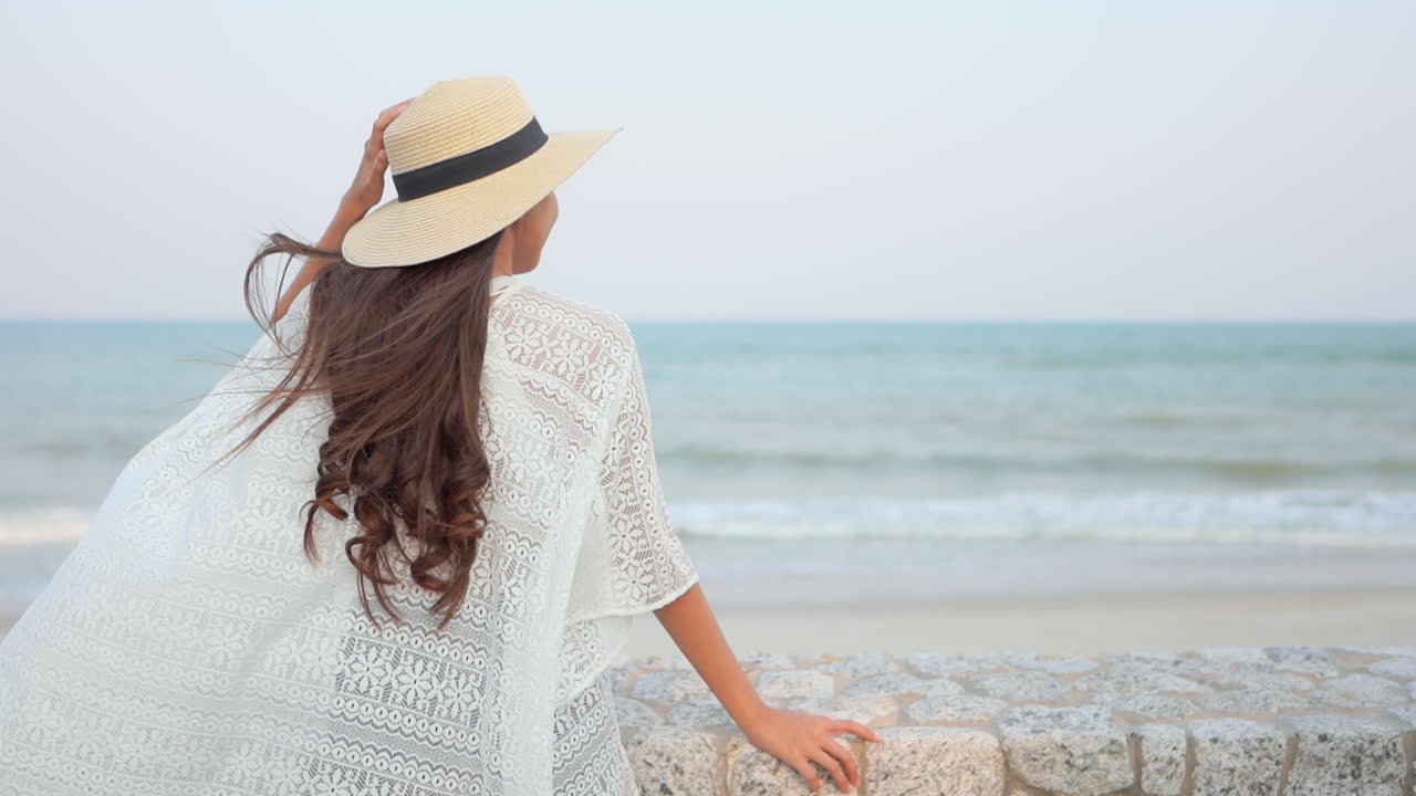 Rear view of long haired woman looking at the sea in beach dress, enjoy breeze