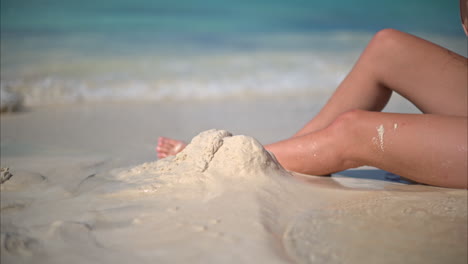 Mujer-Caucásica-Bronceada-Sentada-En-La-Playa-Jugando-Con-Arena-Mojada-En-Un-Día-Soleado-En-El-Caribe