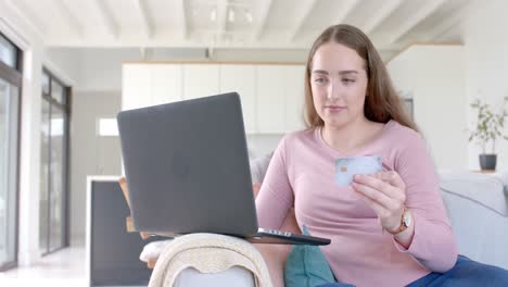 mujer caucásica feliz usando una computadora portátil y una tarjeta de crédito en cámara lenta