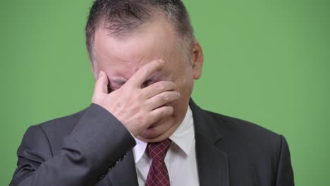 mature sad japanese businessman crying while covering eyes