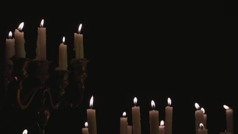 a group of white candles some on a candelabra lit up and running for a while