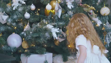 girl-tries-to-get-gift-from-under-Christmas-tree-in-room