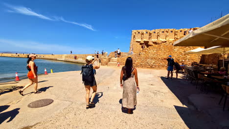 tourists and foreigners walking along the coasts and beaches of chania in crete, greece while looking at the ancient and colorful buildings and taking pictures