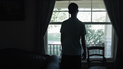 Cinematic-shot-of-a-sad-young-teenage-boy,-high-school-aged-young-man-with-depression-and-anxiety-looking-out-window-sadly