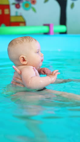 trainer holds a baby in the swimming pool on the straight hands. coach deeps a child's face into water learning him to swim. vertical video.