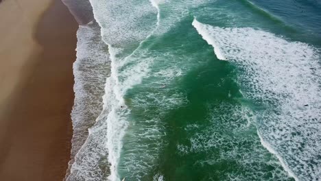 Vista-Aérea-De-La-Playa-De-Arena-En-Hossegor-Francia-Con-Olas-Oceánicas-Rompiendo-En-La-Orilla-Y-Surfistas-Remando-Hacia-La-Fila